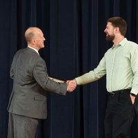 Doctor Potteiger shaking hands with an award recipient in a pastel green shirt